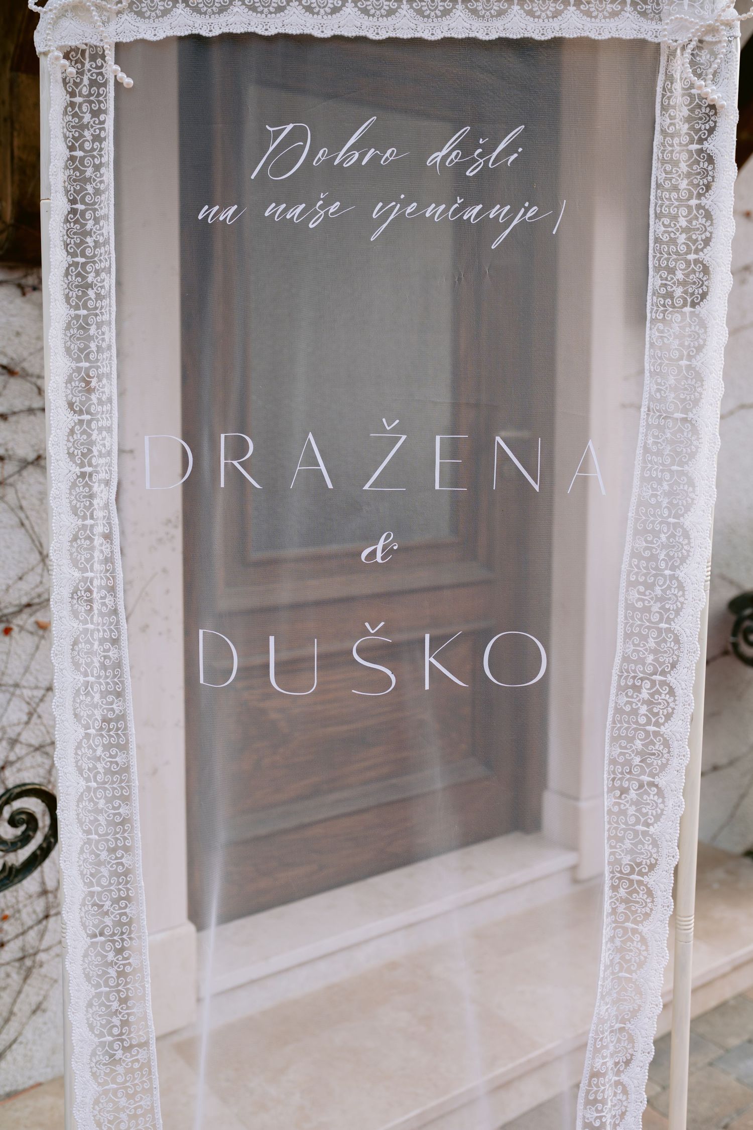 White lace curtains frame a window display with elegant text lettering visible through the glass.