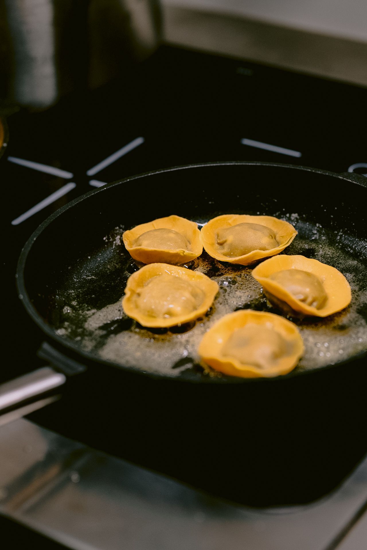 Yellow ravioli pasta being pan-fried in a black skillet.