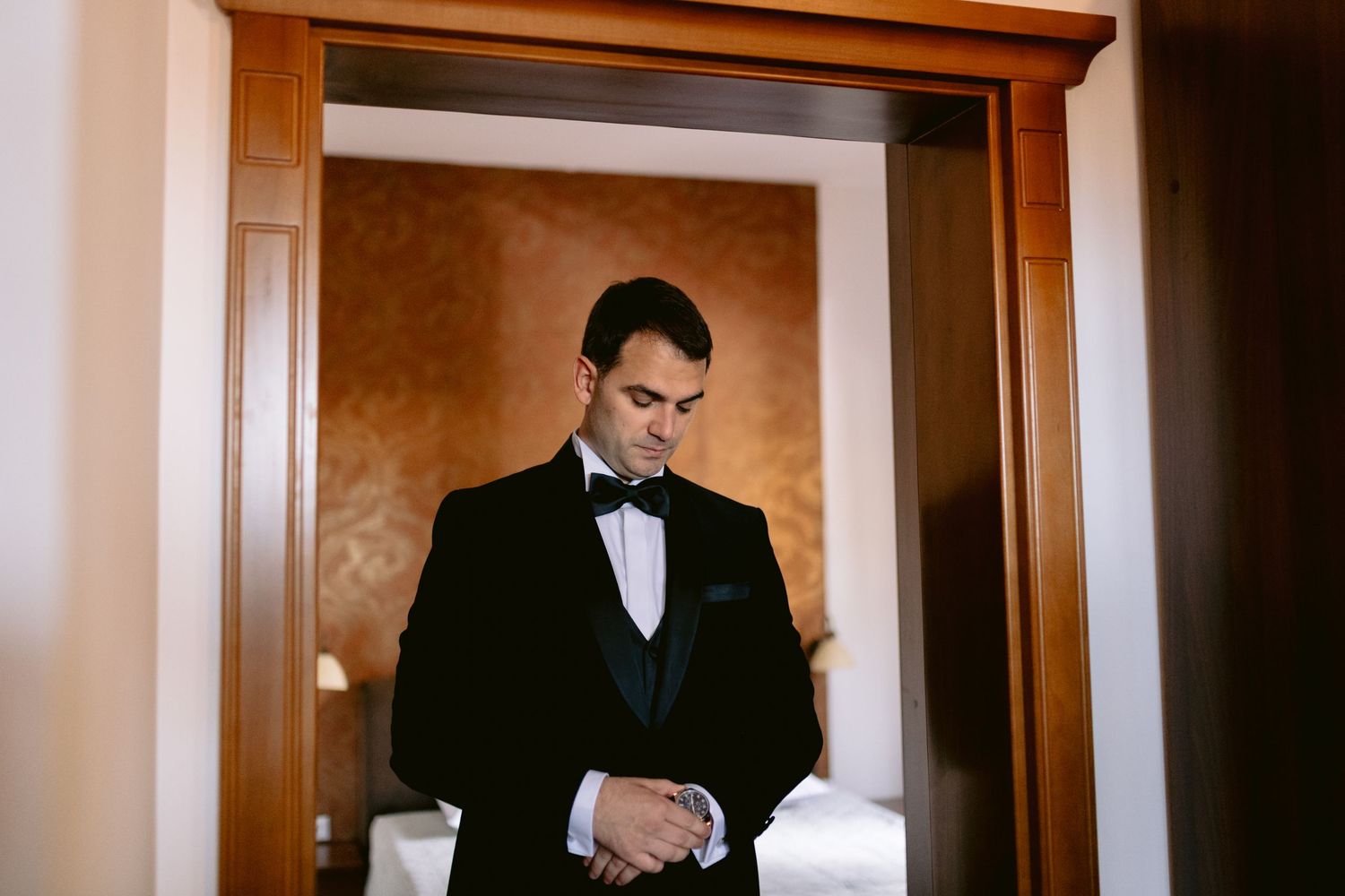 Groom in a black tuxedo making final adjustments before the wedding ceremony.
