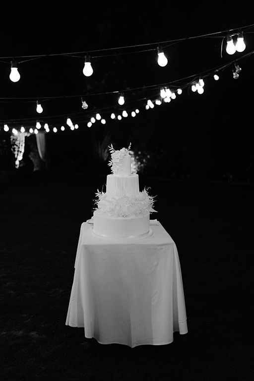 Wedding cake display under string lights creating a romantic evening atmosphere.