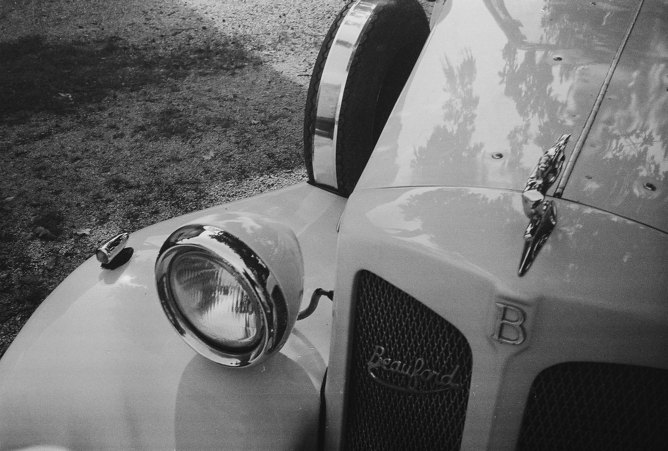 Detalj prednjeg dijela retro Bentley automobila sa prikazom klasičnog fara i kultnog B ukrasa na haubi.