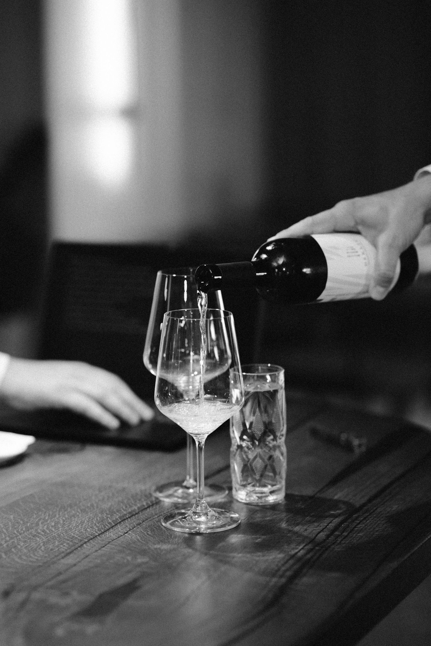 Black and white photo of wine glasses and water glasses on a rustic wooden table in moody lighting in belgrade resoran
