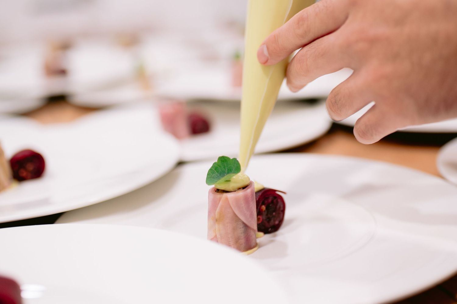 A close-up view of hands plating a gourmet dish with garnishes and sauces on a white plate.