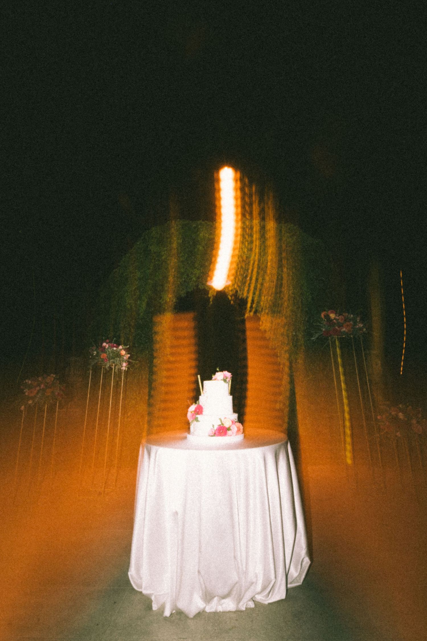 Long exposure night photograph shows glowing light trails around a white draped table creating an ethereal effect.