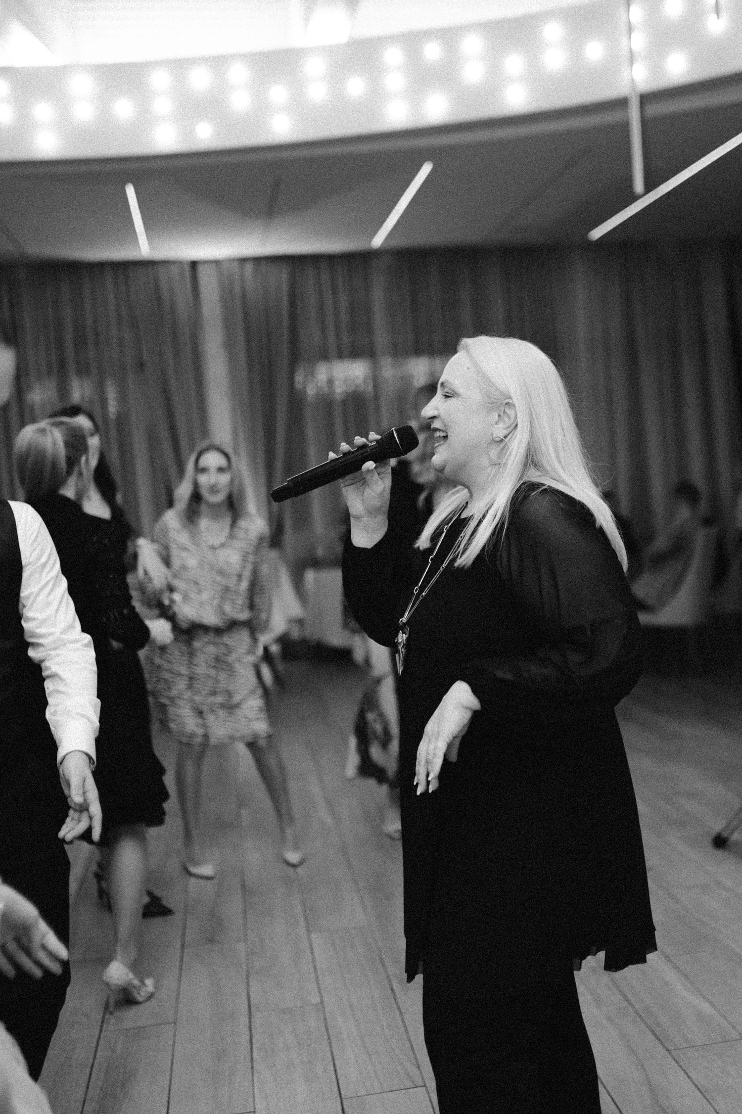 Blonde woman singing into microphone at wedding reception in black and white photo.