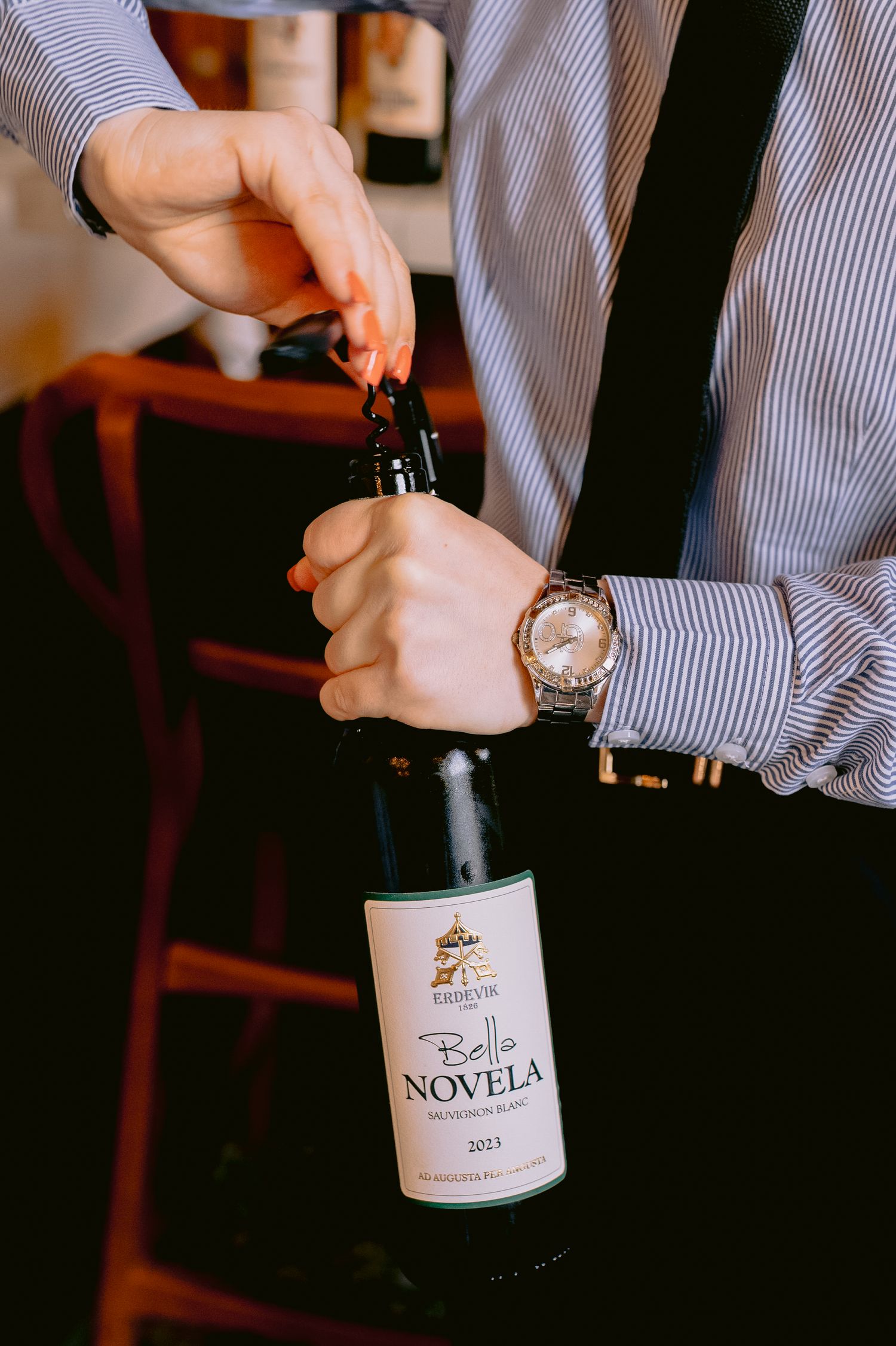 Someone in a striped shirt opening wine bottles at a restaurant.