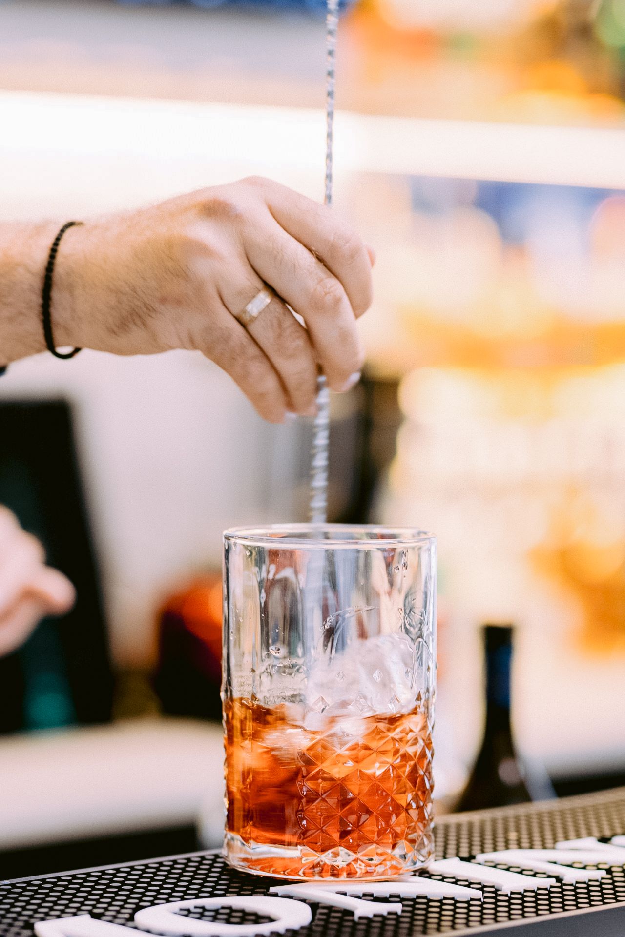 Bartender pouring an amber-colored cocktail into a crystal glass at an upscale bar.