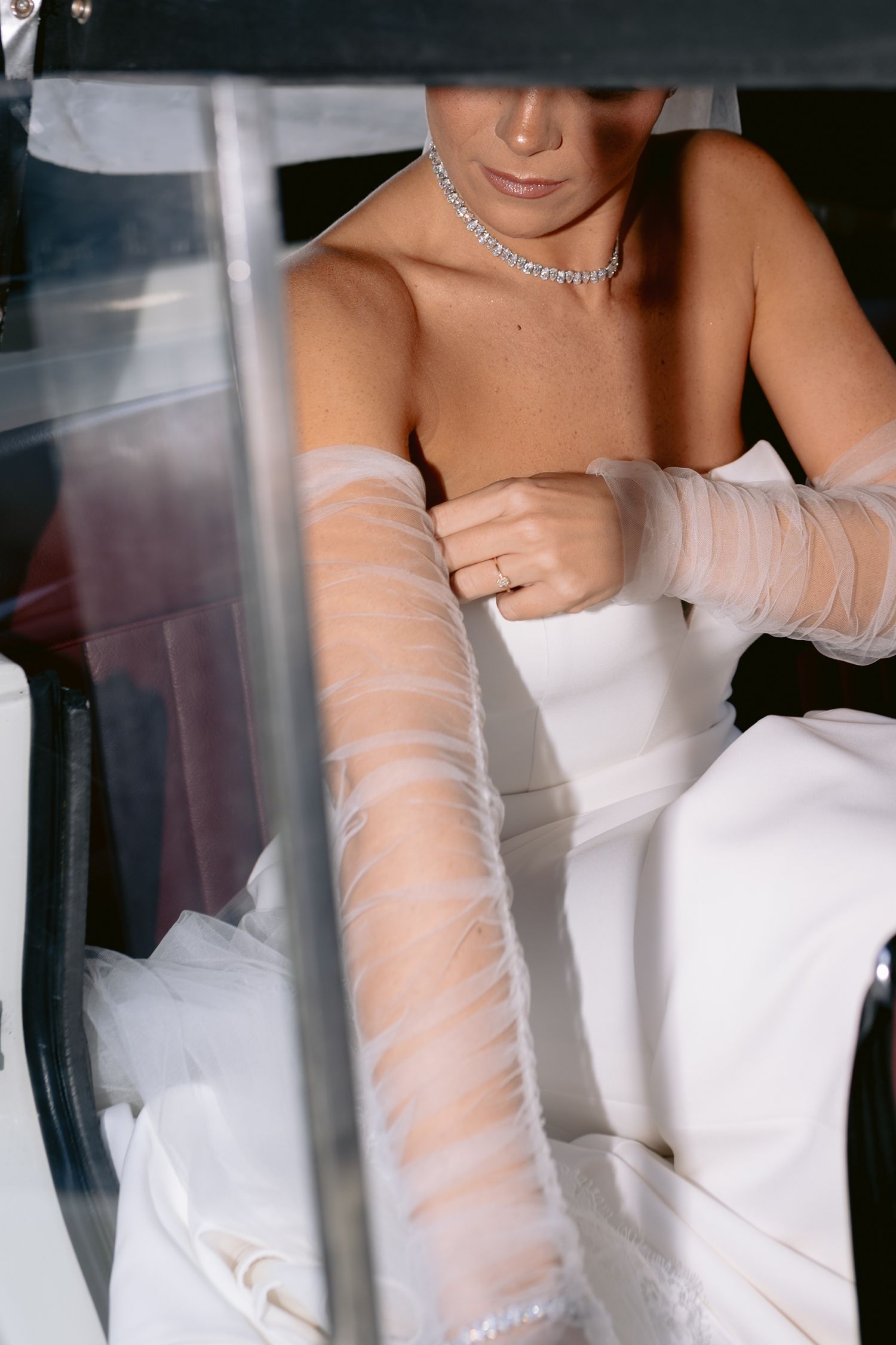 Close-up details of elegant sheer white gloves with delicate ruching texture against a bridal gown.