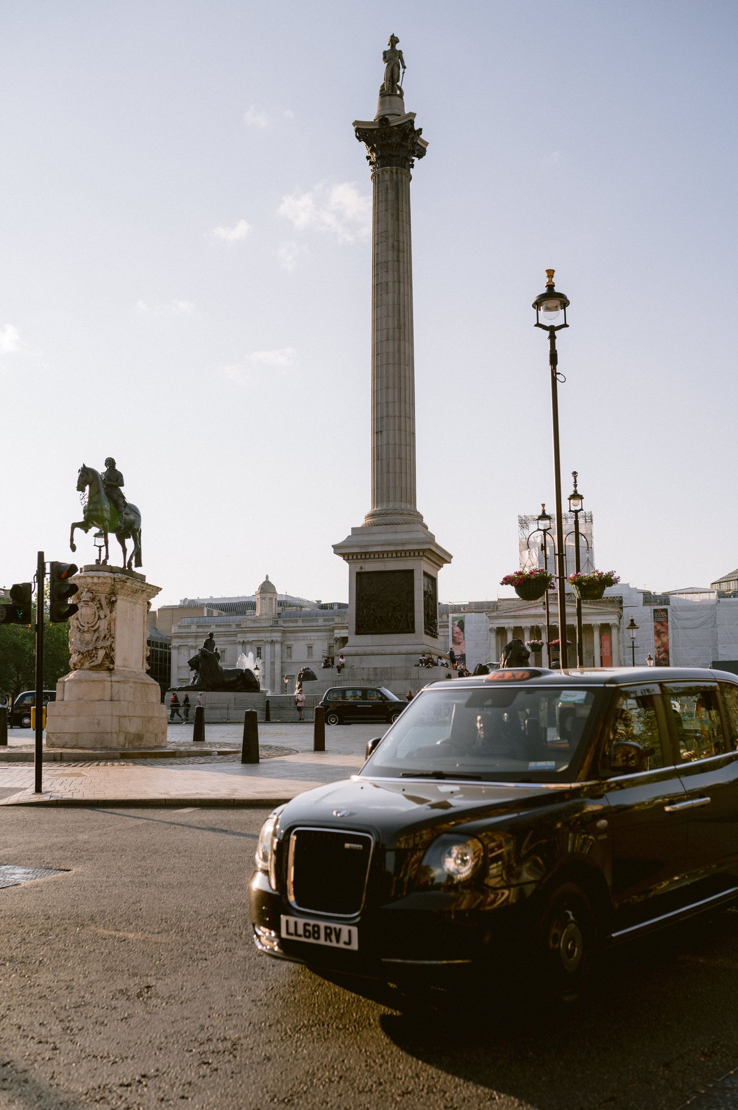 Rolls Royce luxury car parked near historic stone columns and monuments in a European city square at dusk.