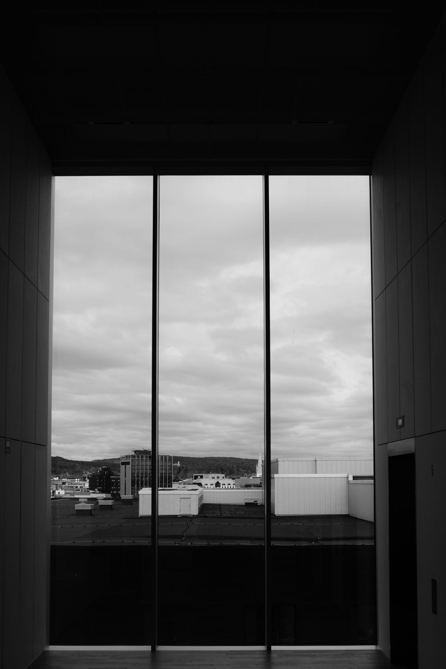 Black and white architectural photograph showing a window view of a cloudy cityscape with geometric framing elements.