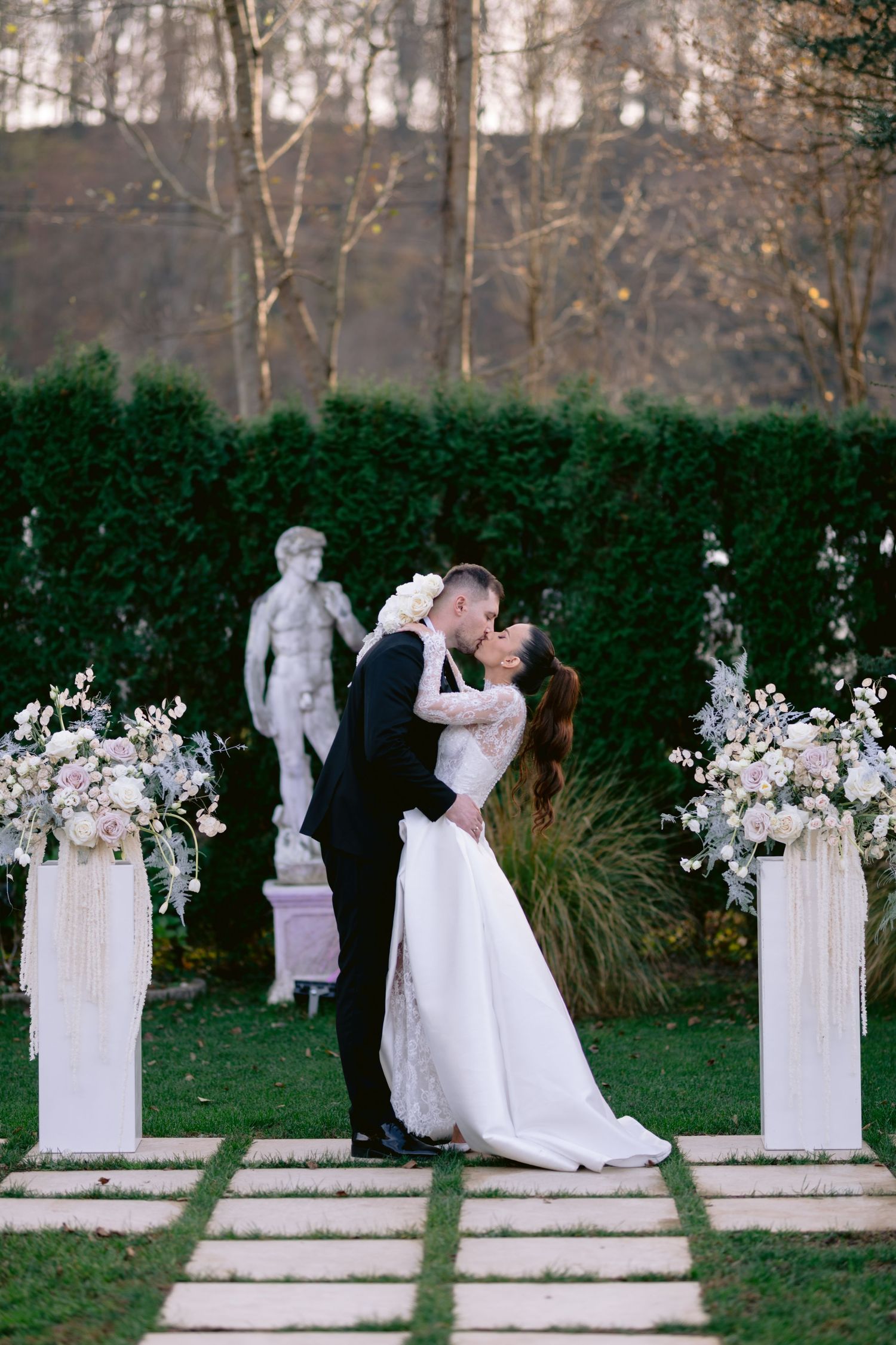 A romantic wedding photo sequence showing a couple in a garden with white floral arrangements and classical statues.
