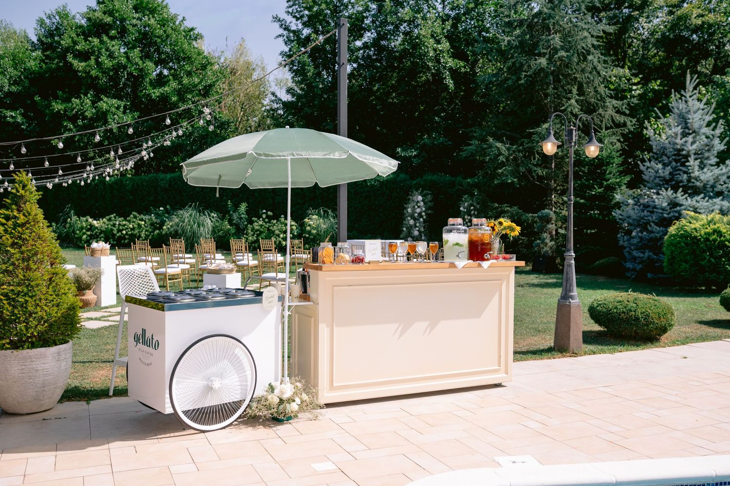 Outdoor wedding reception setup with white tables and umbrellas surrounded by lush greenery.