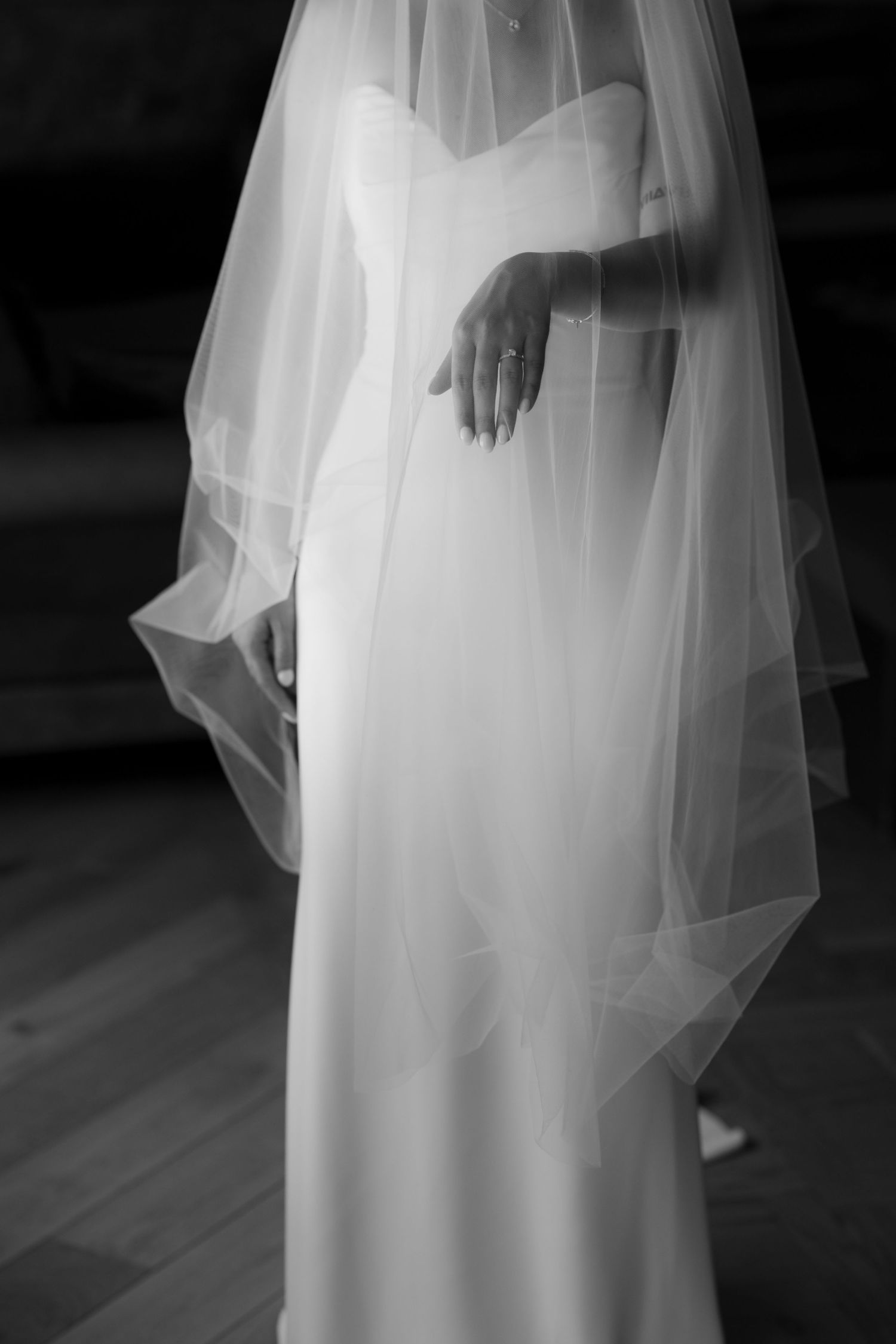 Black and white detail of a bride's wedding dress with flowing veil.