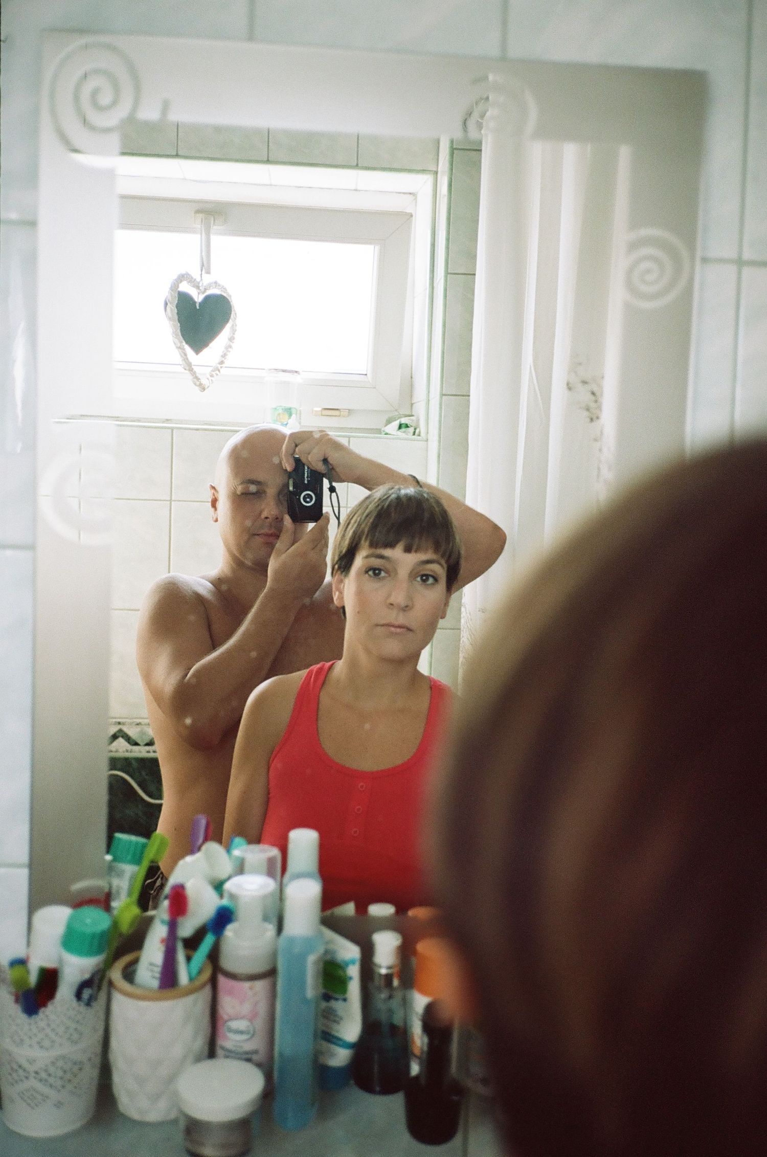 A bathroom mirror reflection shows someone styling hair while various toiletries and beauty products line the counter below.