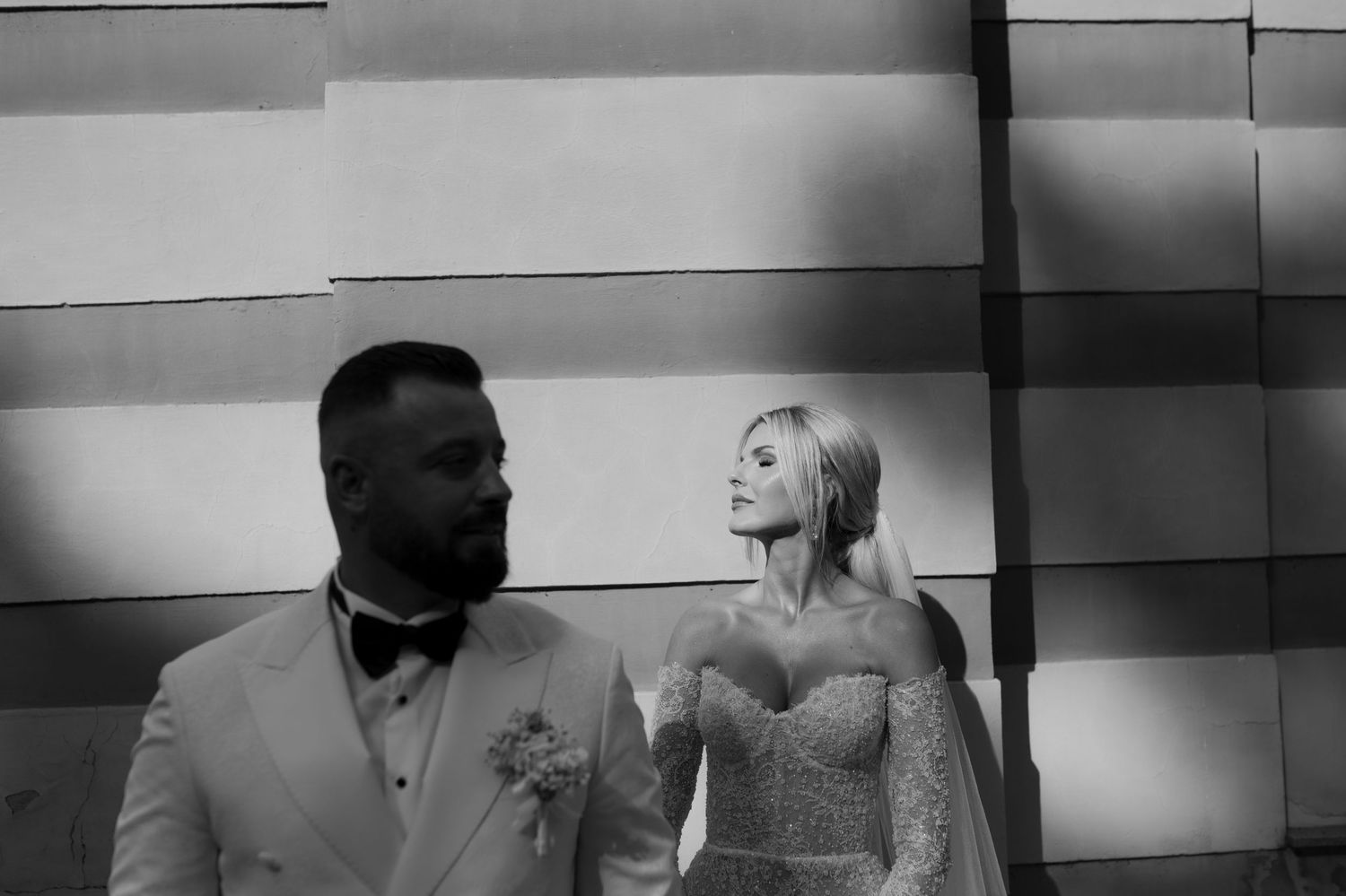 Black and white portrait of wedding couple sharing an intimate moment against geometric wall.