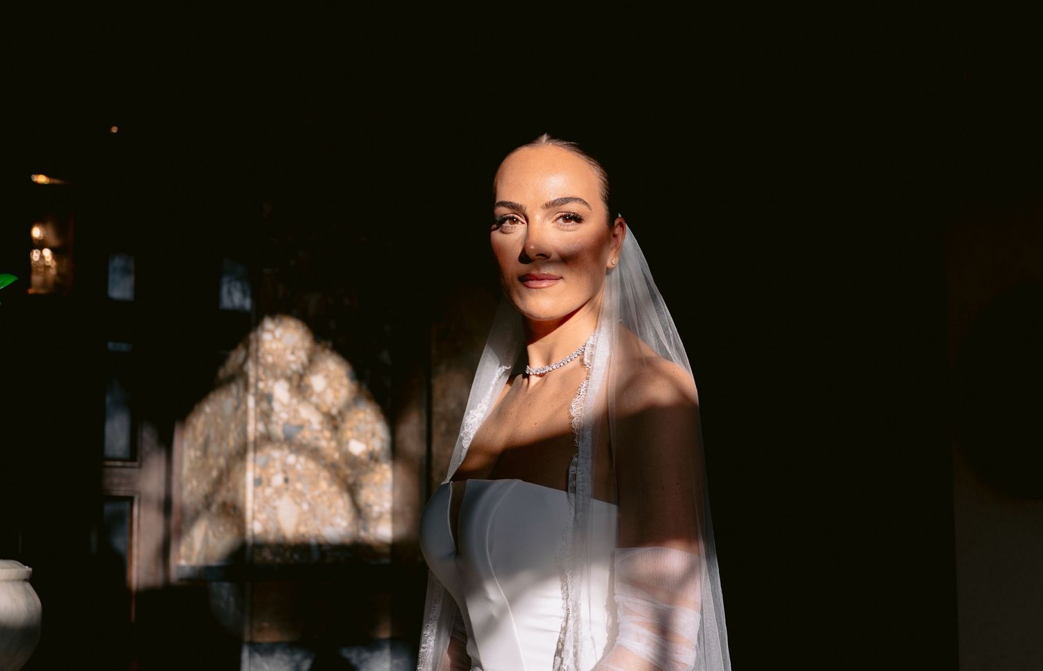 A person in a white wedding dress poses in dramatic shadows and lighting during a bridal photoshoot.
