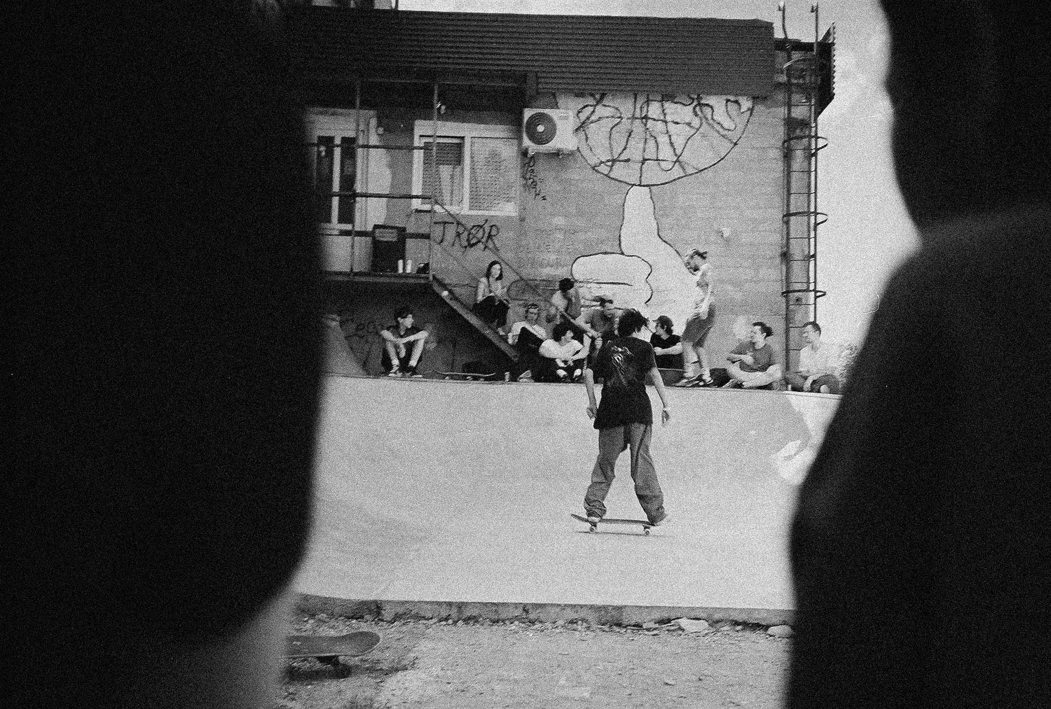 A skateboarder performs a trick on a concrete ledge in a black and white urban setting.
