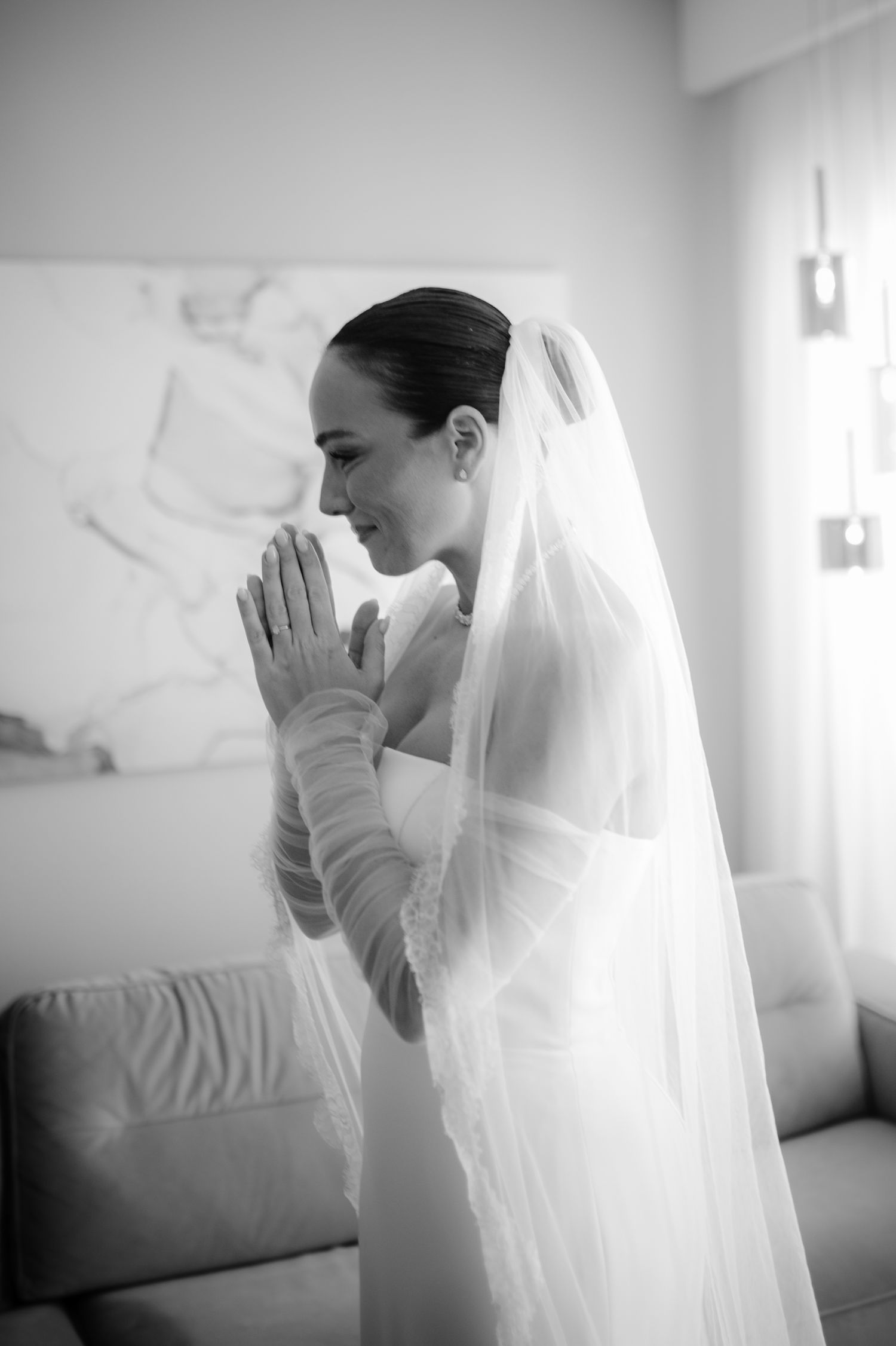 Black and white photo of a smiling bride in a veil and gloves, hands clasped in prayer on her wedding day.