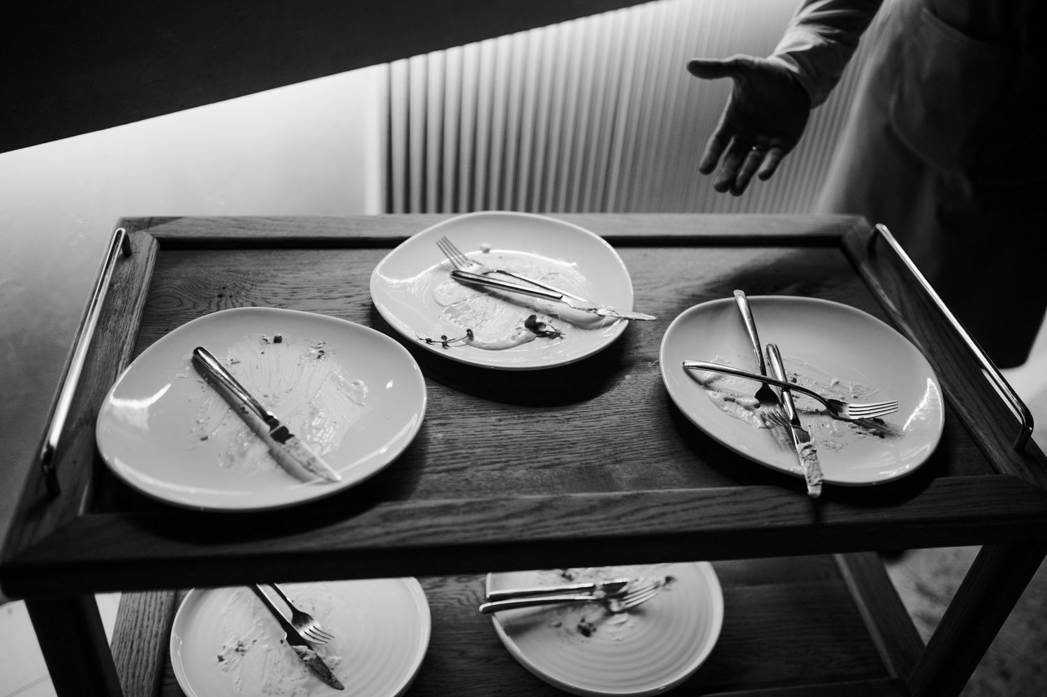 Black and white image shows empty plates and utensils on a wooden table after a meal.
