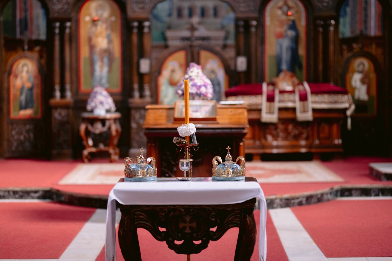 Ornate cathedral interior with red carpeting, wooden pews, and stained glass windows illuminated in warm lighting.