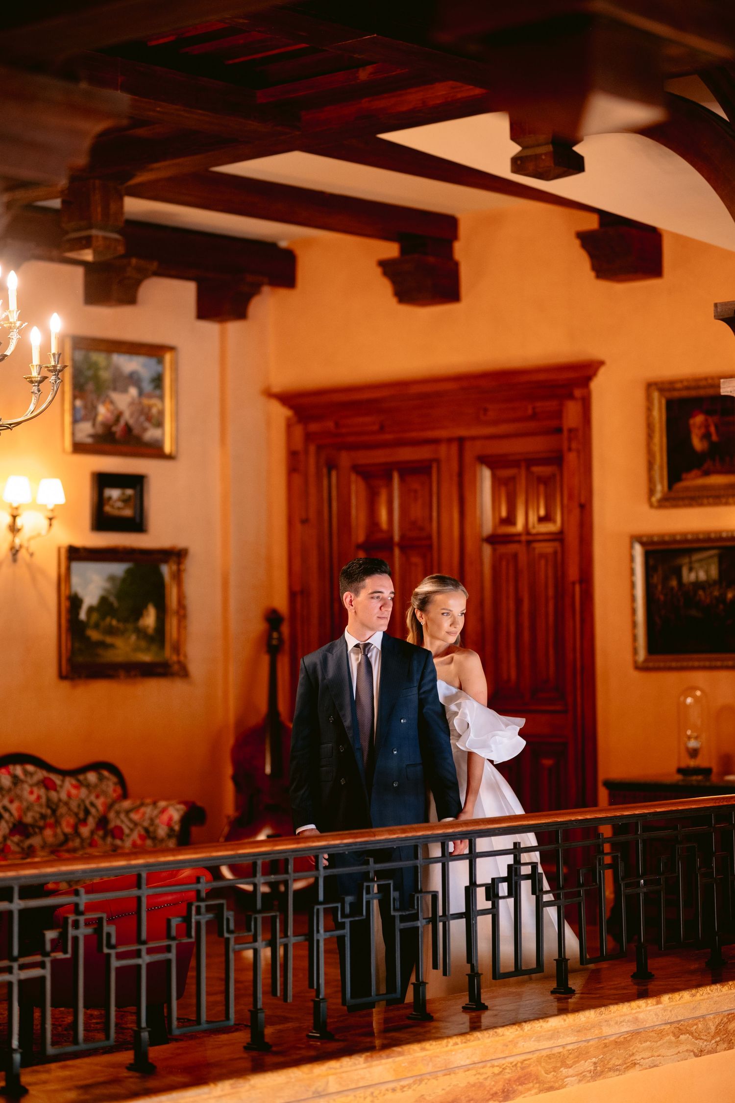 Wedding couple posing along an ornate railing in a warmly lit historic interior.