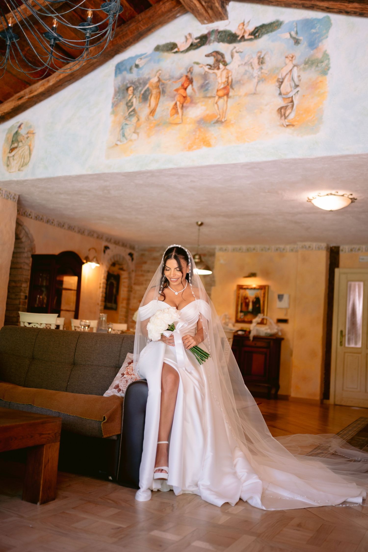 Mlada u vjenčanici pozira u elegantnoj prostoriji sa dekorativnim zidnim slikama.