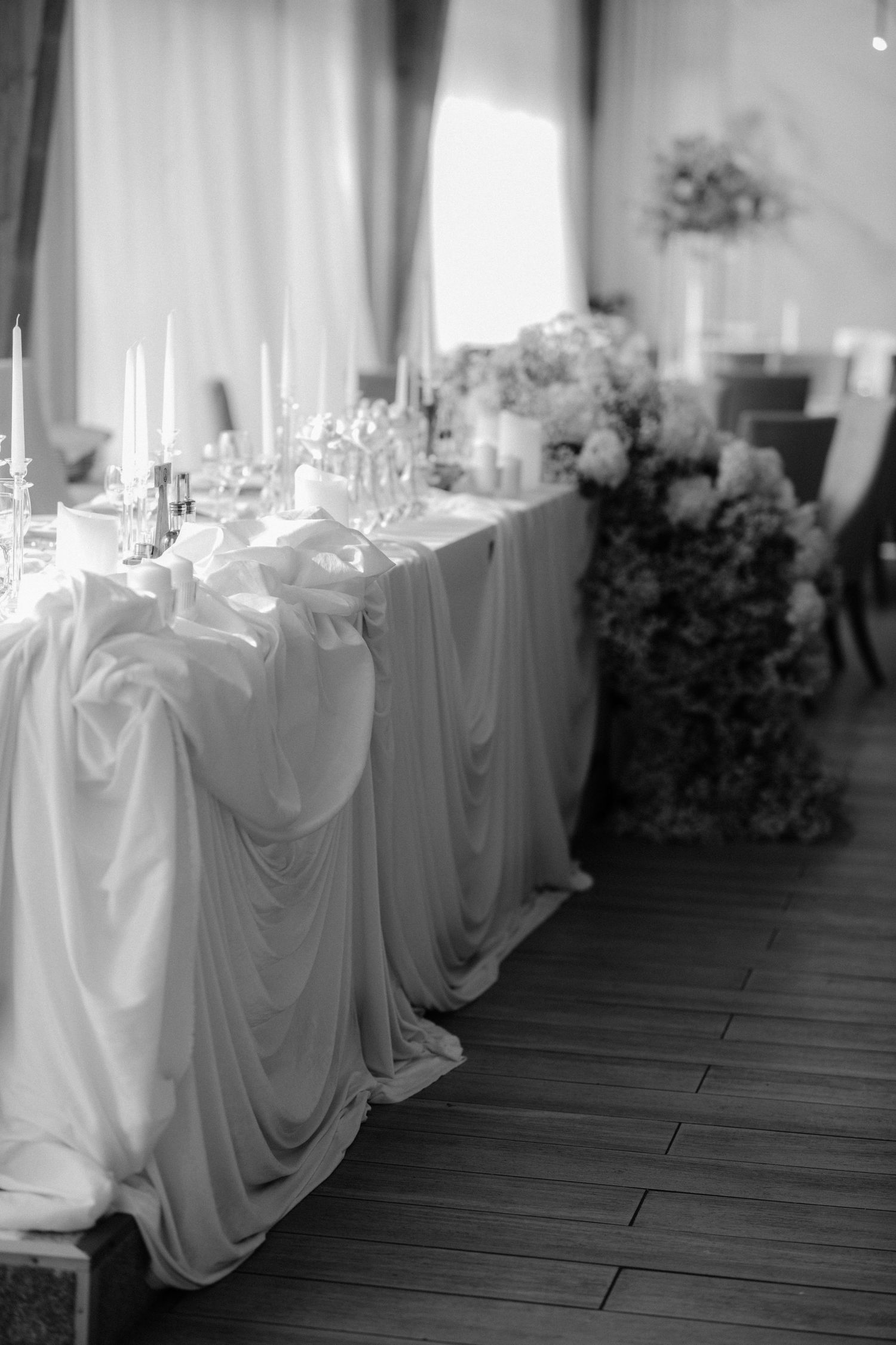Black and white photo of an elegant wedding reception table with draped white fabric, candles, and floral arrangements.