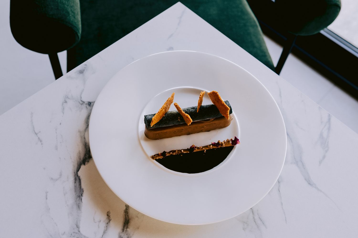 Elegant plated chocolate dessert with caramel garnish on white marble table in upscale restaurant setting.