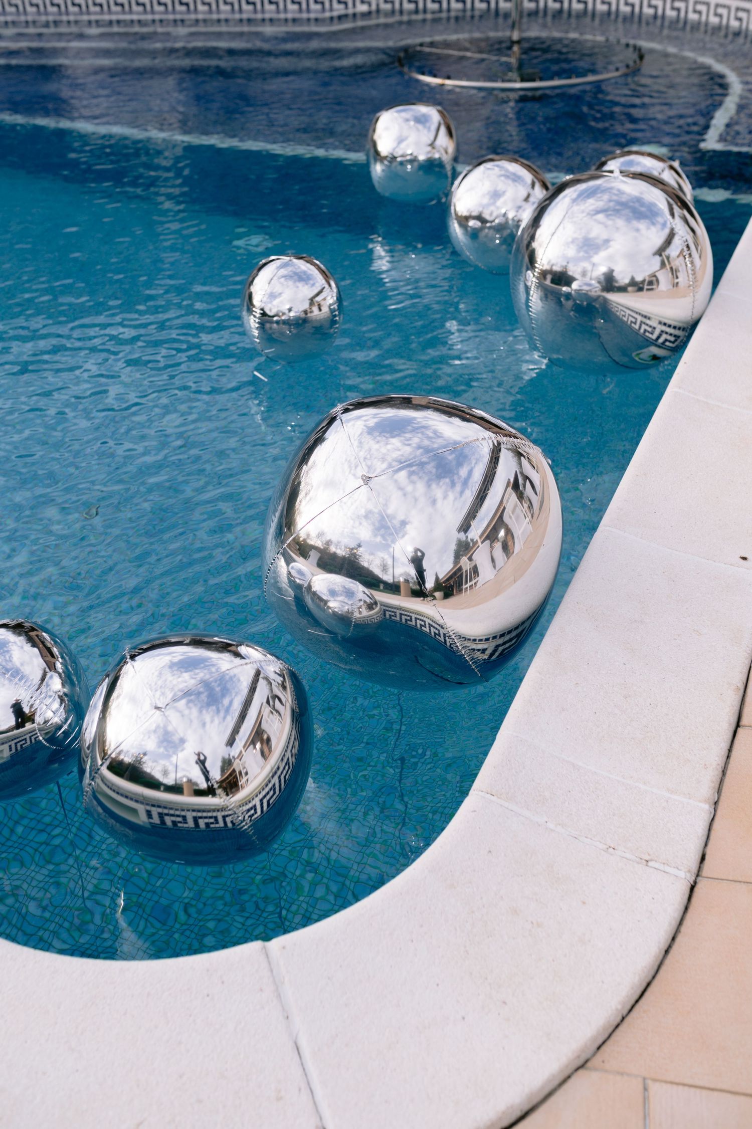 Swimming pool with silver inflatable pool pillows floating on bright blue water against white curved pool edge.