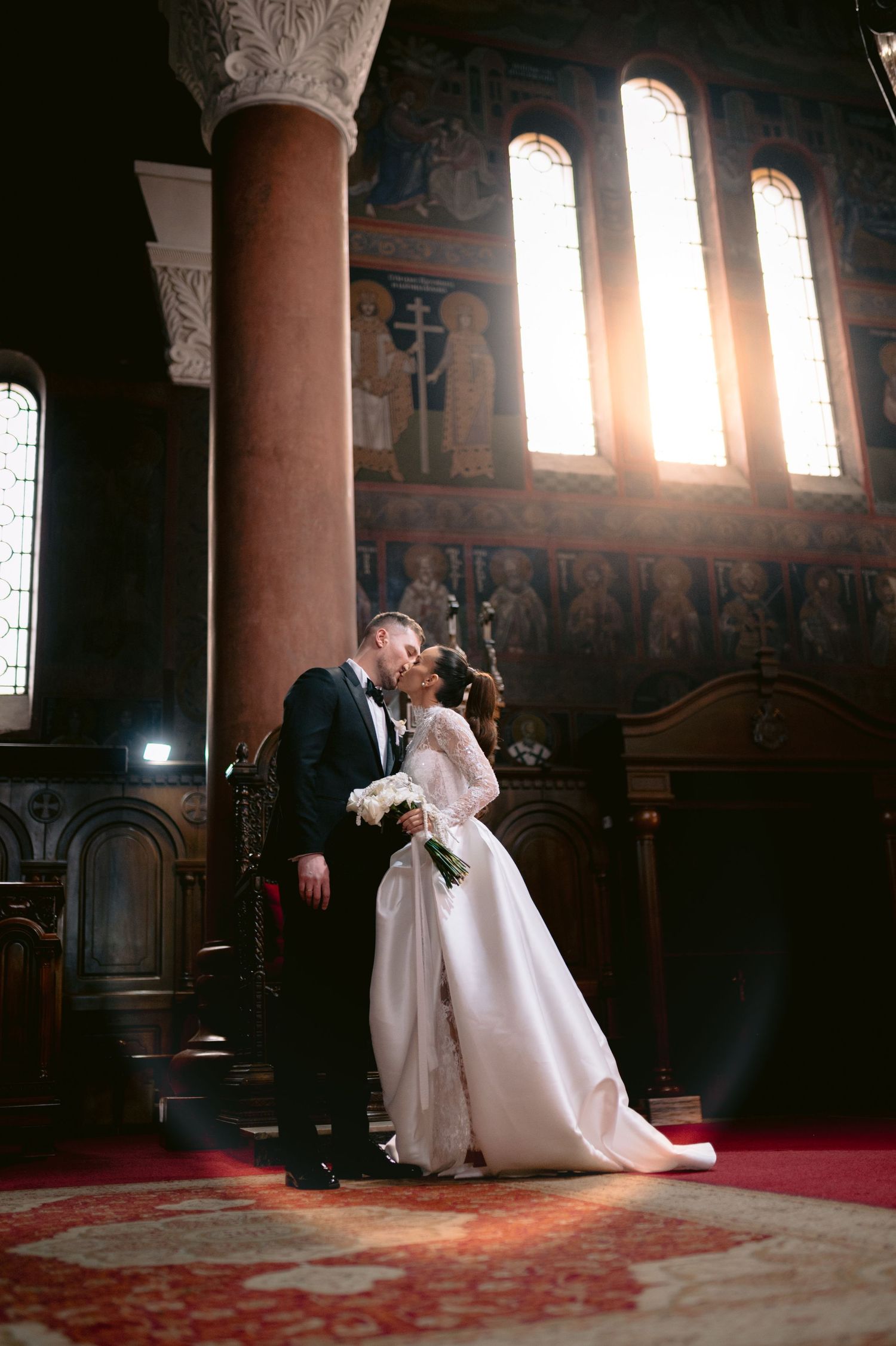Dramatic church wedding photos with sunlight streaming through stained glass windows onto couple.