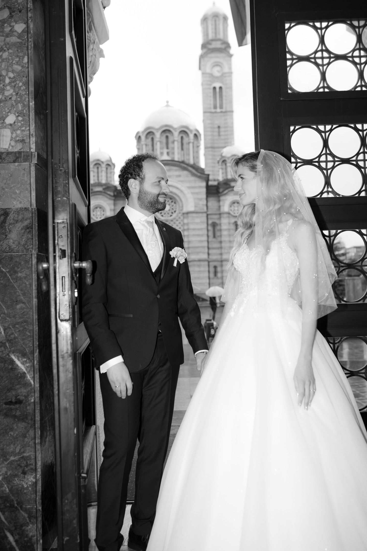 Black and white photos of a bride and groom standing together in front of ornate church windows.