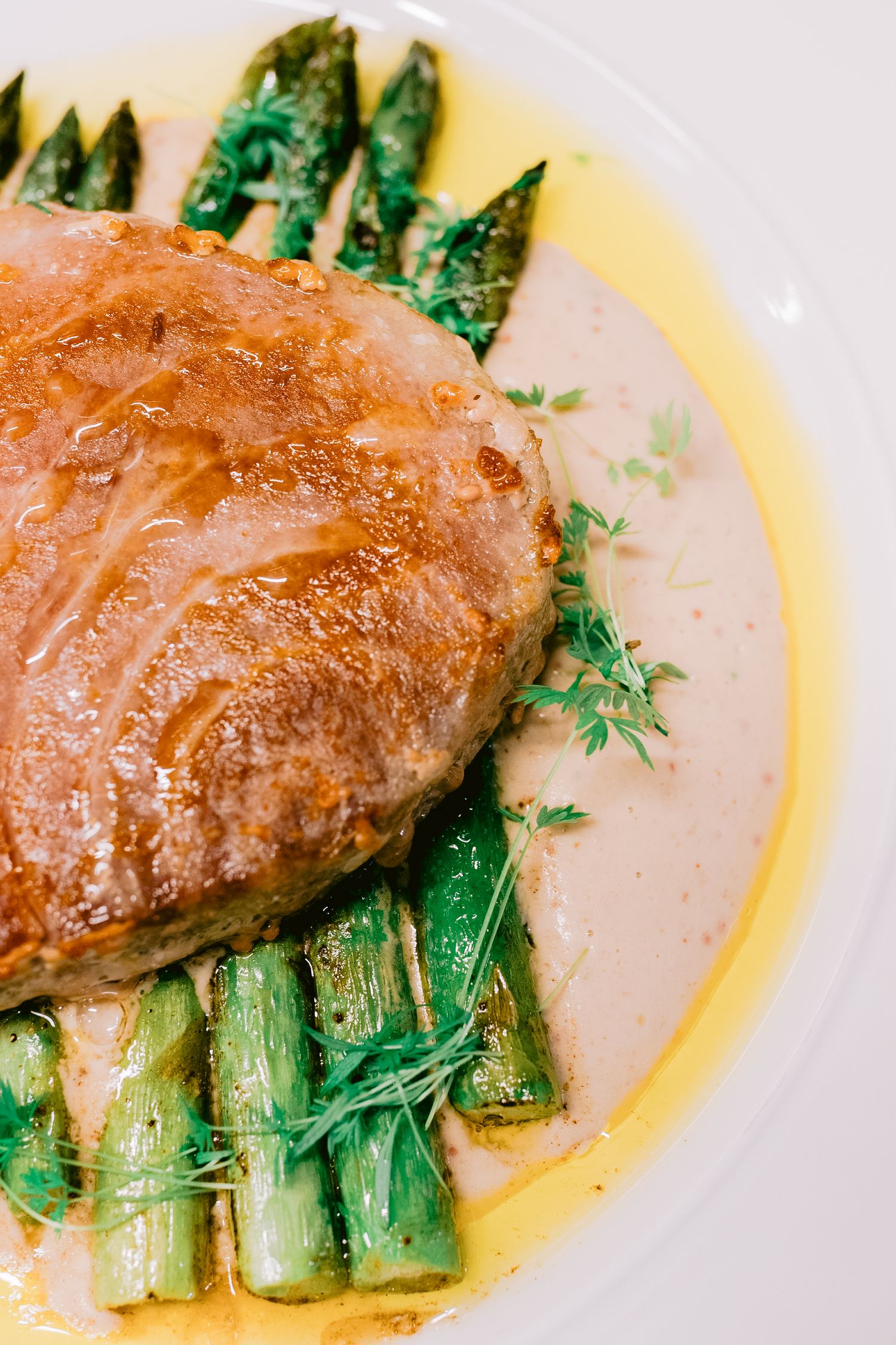 Seared fish fillet served over grilled asparagus with butter sauce.
