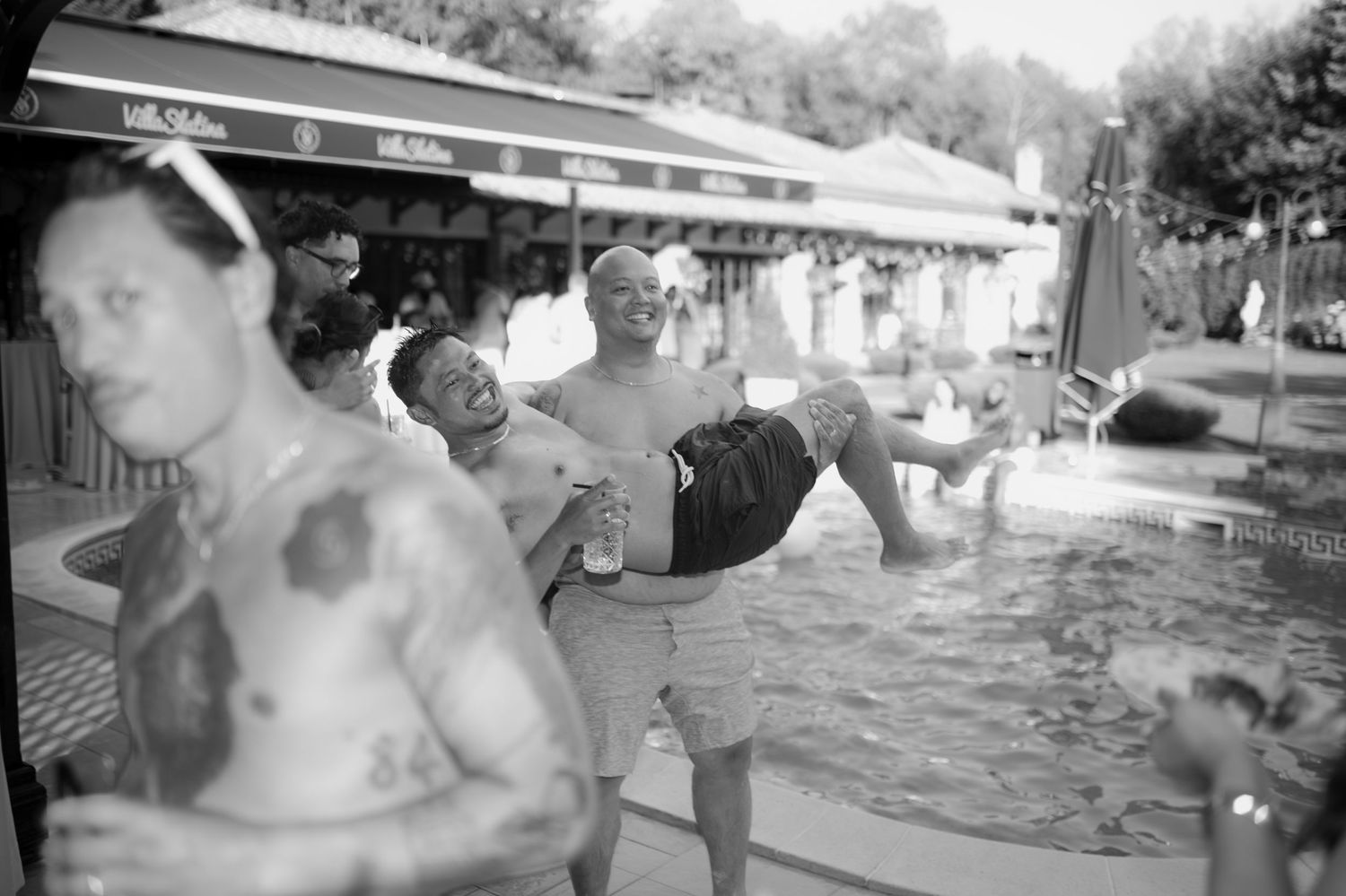 Crno-bijela fotografija gostiju kako bacaju prijatelja u bazen na pool party vjenčanju, Villa Slatina Banja Luka