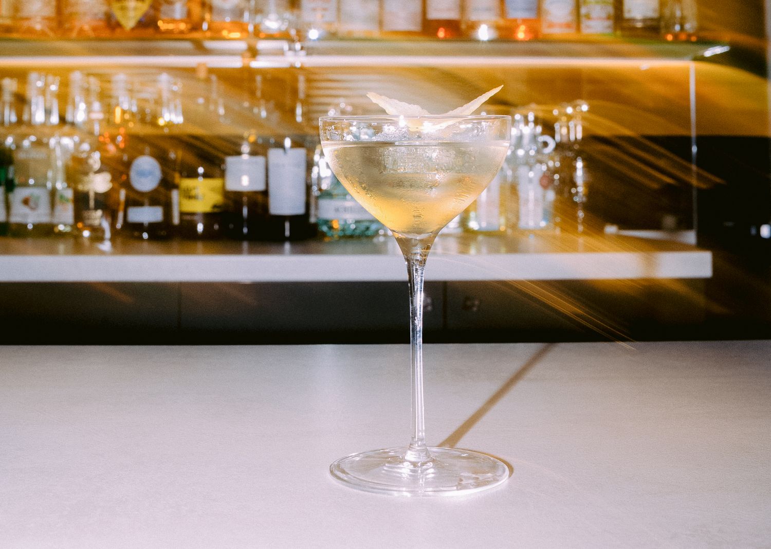 Elegant cocktail glasses lined up on a bar counter with warm lighting.