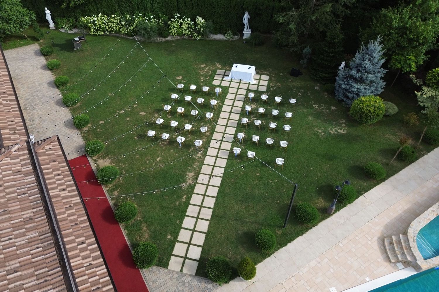 Fotografija slikana dronom ceremonija vjenčanja na otvorenom sa bijelim stolicama i kamenom stazom u vrtu pored bazena u Villi Slatina.