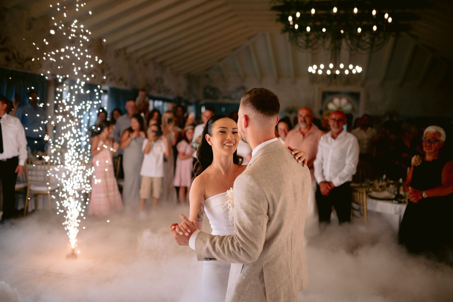 Newlyweds share their first dance surrounded by sparklers on a misty dance floor.