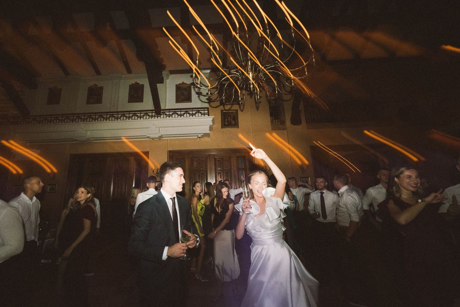 Wedding guests dance together on a dimly lit dance floor during an evening reception celebration.
