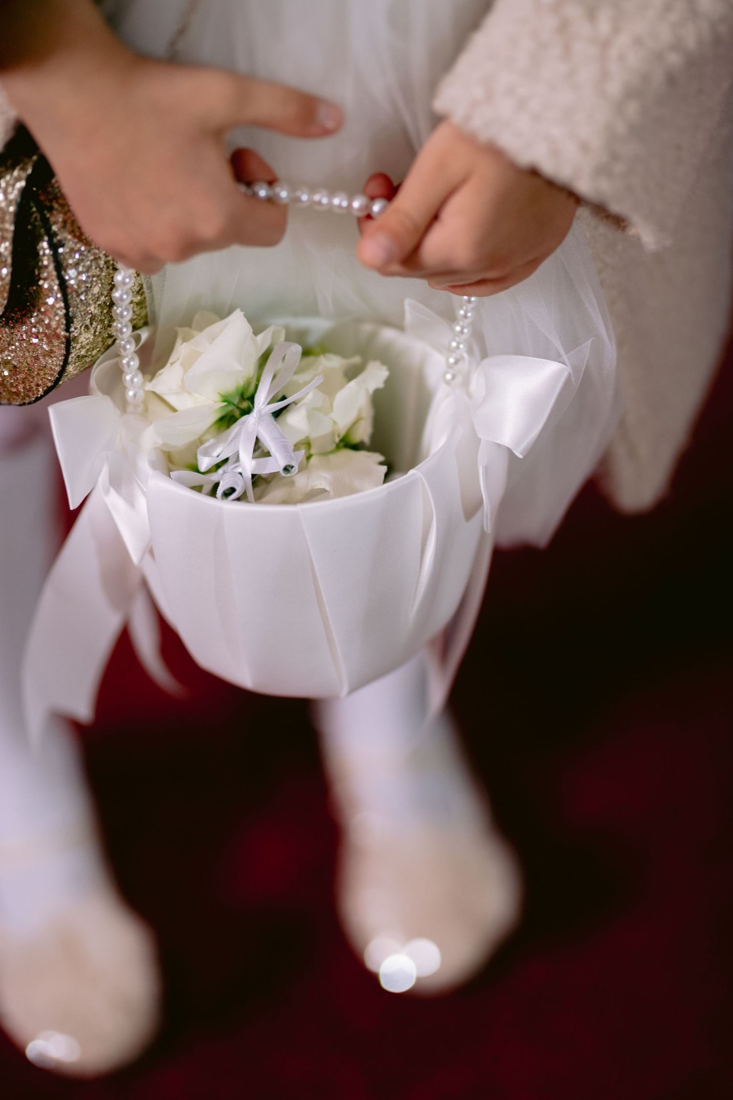 Hands adjusting a delicate pearl bracelet above a white floral bouquet wrapped in elegant fabric.