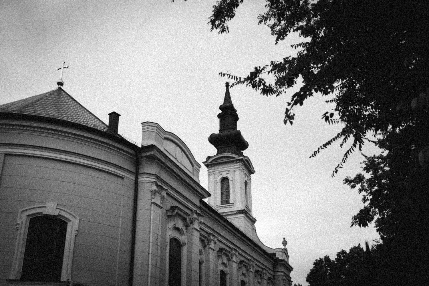Black and white architectural photo of a church exterior with curved walls and ornate steeple against cloudy sky.