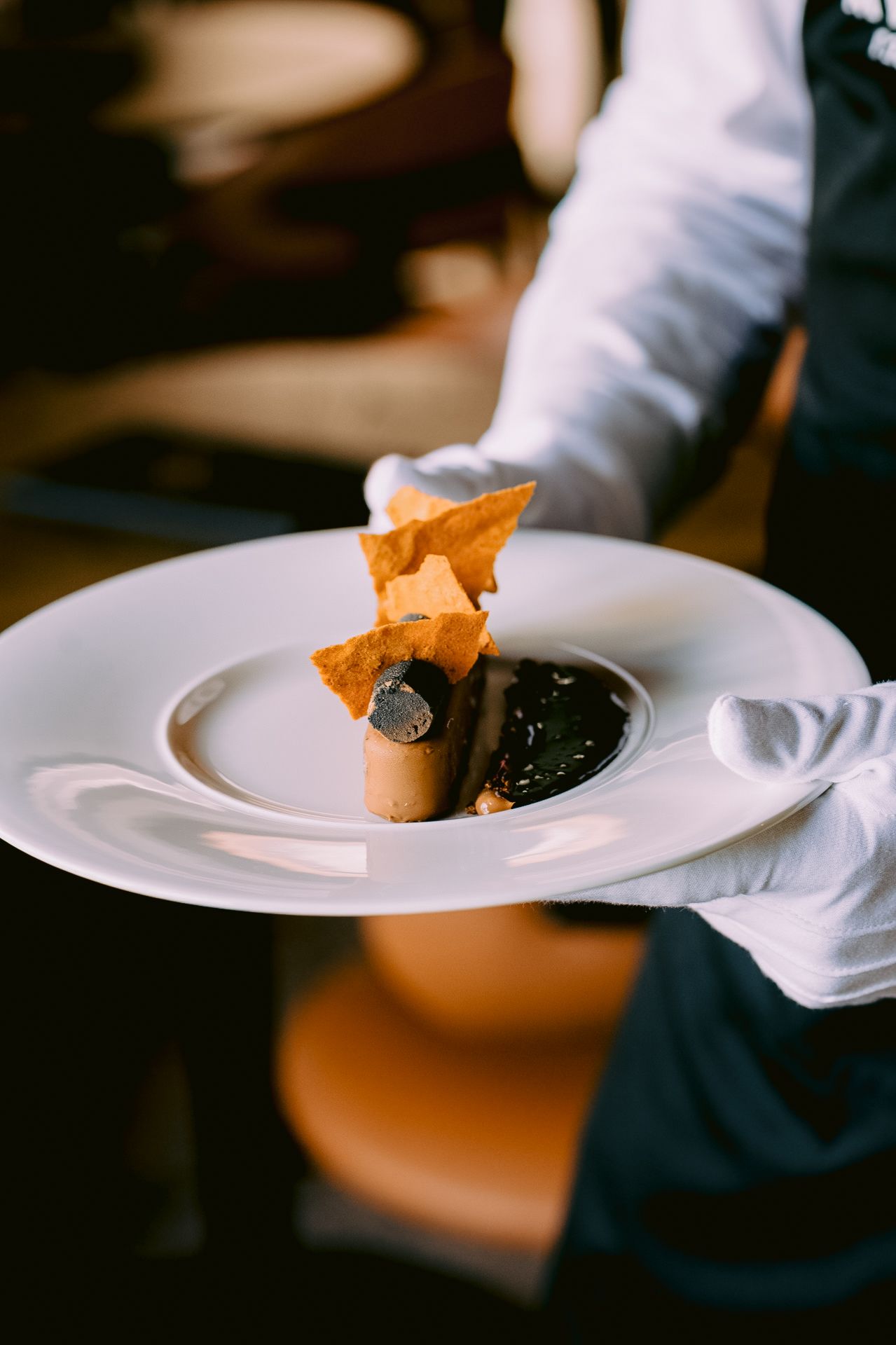 Chef plating a dessert with dark sauce and crispy garnish on white dinnerware.