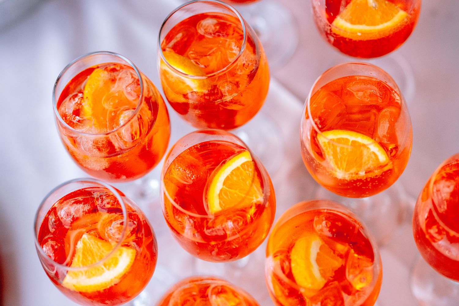 Vibrant Aperol Spritz cocktails garnished with orange slices and ice in stemless wine glasses on a white tray.