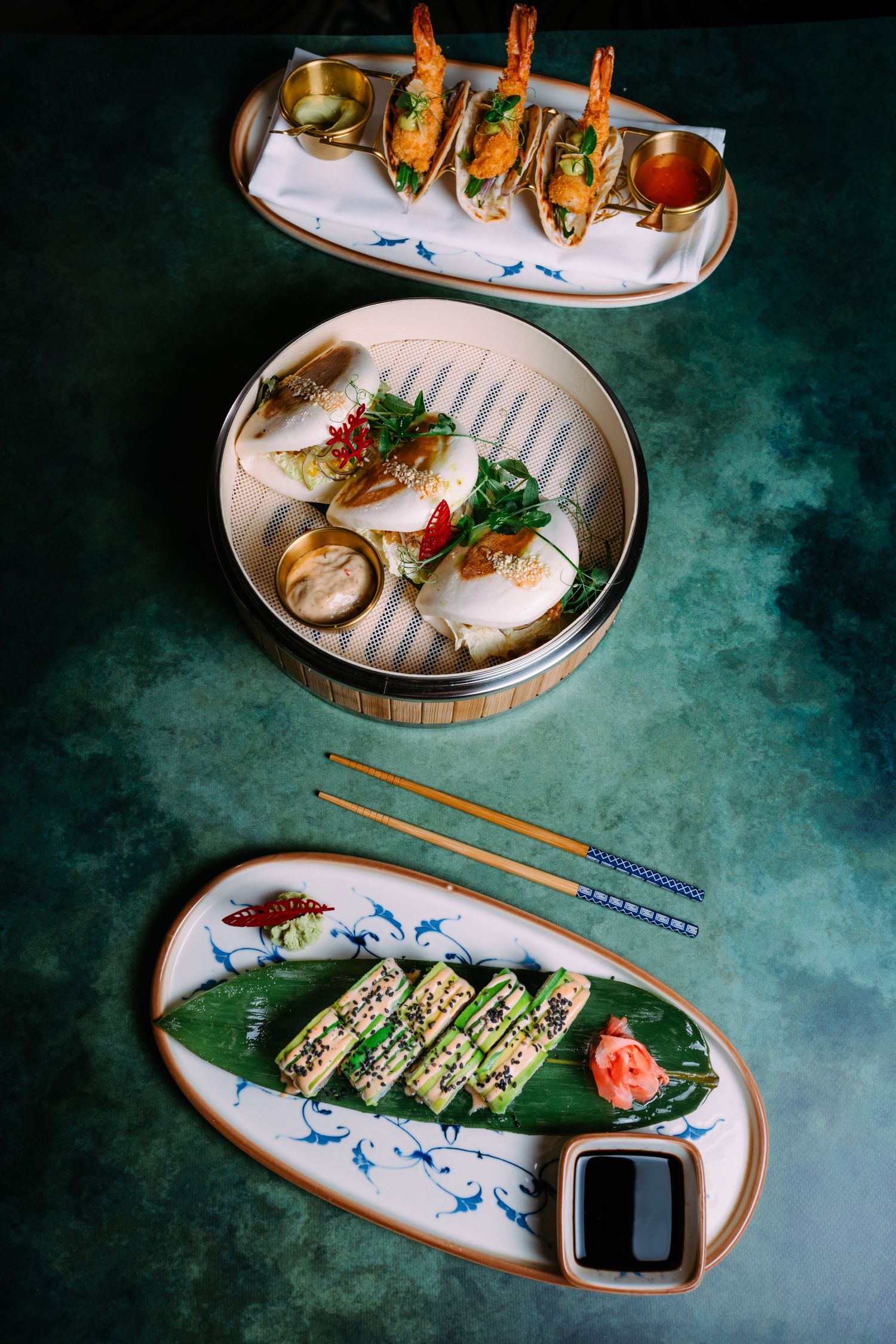 Assorted Asian dishes including dumplings, sushi rolls and seafood served on traditional ceramic plates with chopsticks.