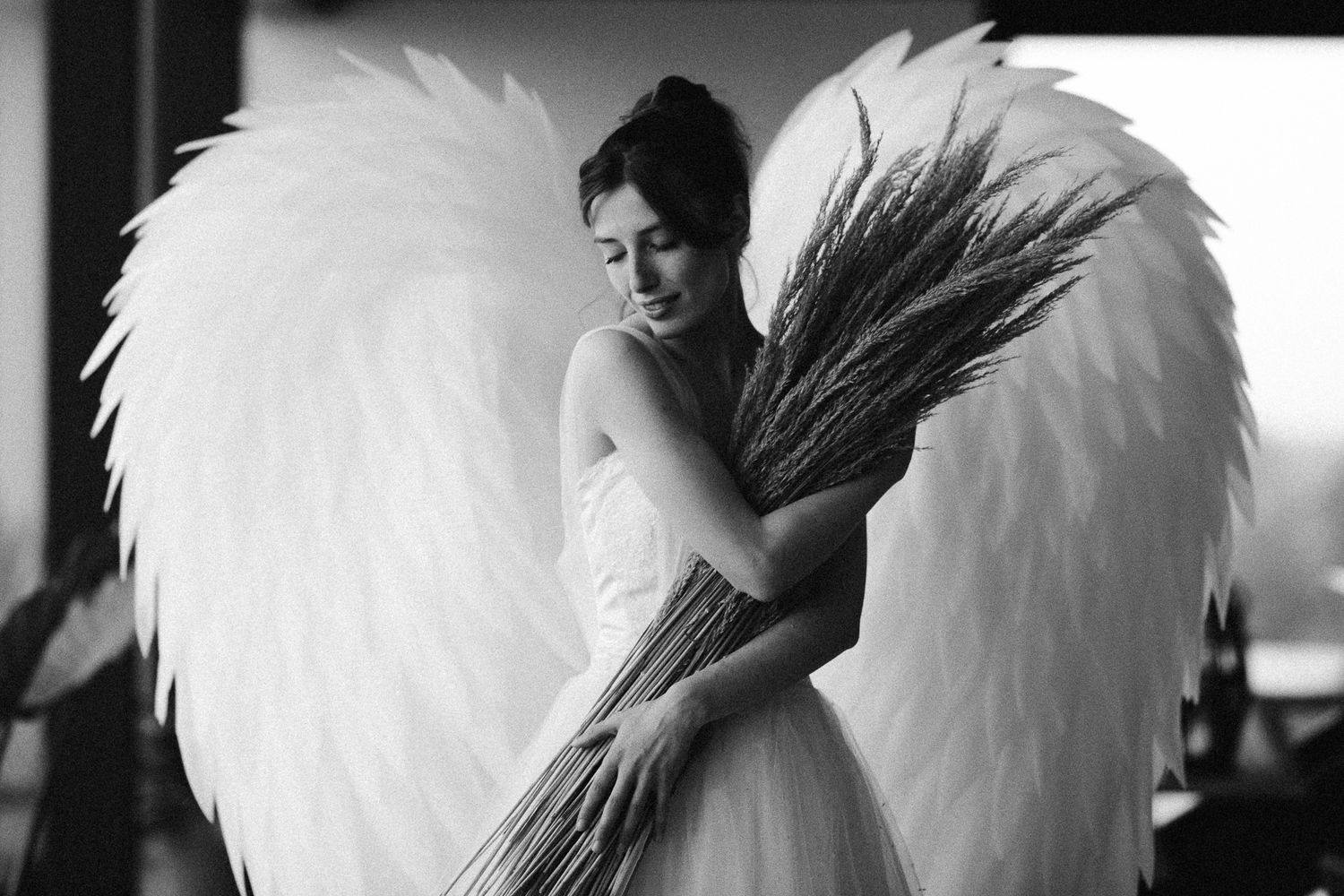 Artistic black and white photo of a bride with large white angel wings.