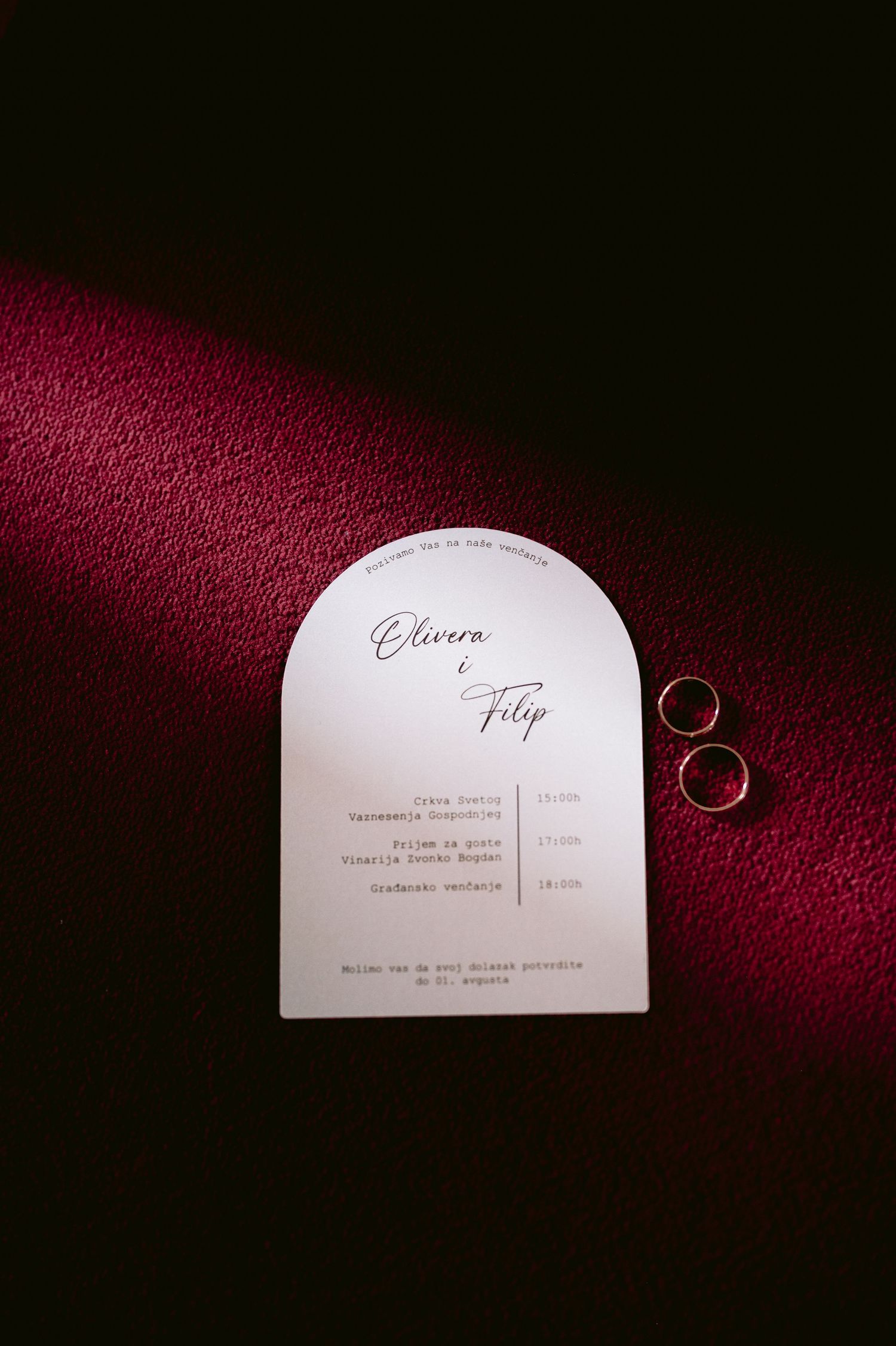 Wedding invitation card and rings on deep red velvet background.