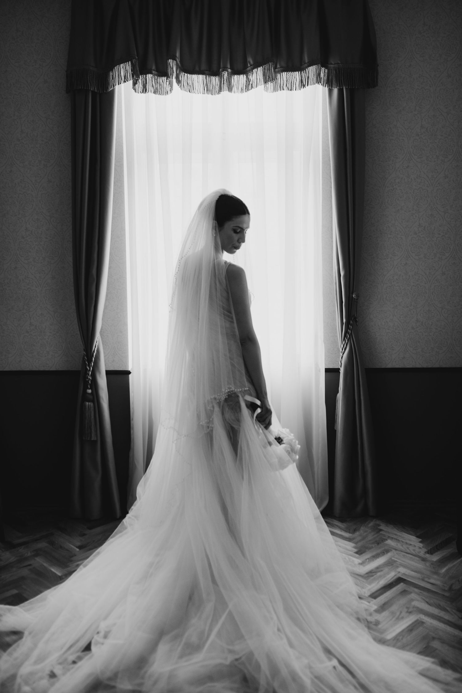 Dramatic black and white silhouette of a flowing wedding dress train against window light.