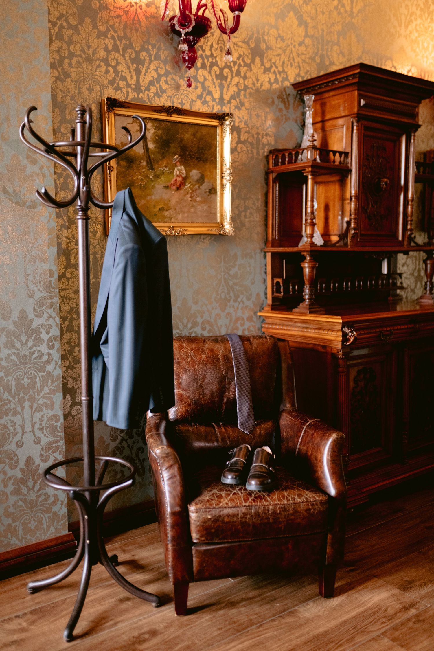 Vintage interior with leather armchair, coat rack, and ornate wallpaper featuring antique furniture and decor.
