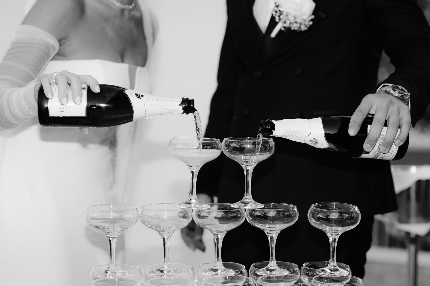 A black and white photo of champagne being poured into a pyramid of elegant coupe glasses at a formal event.