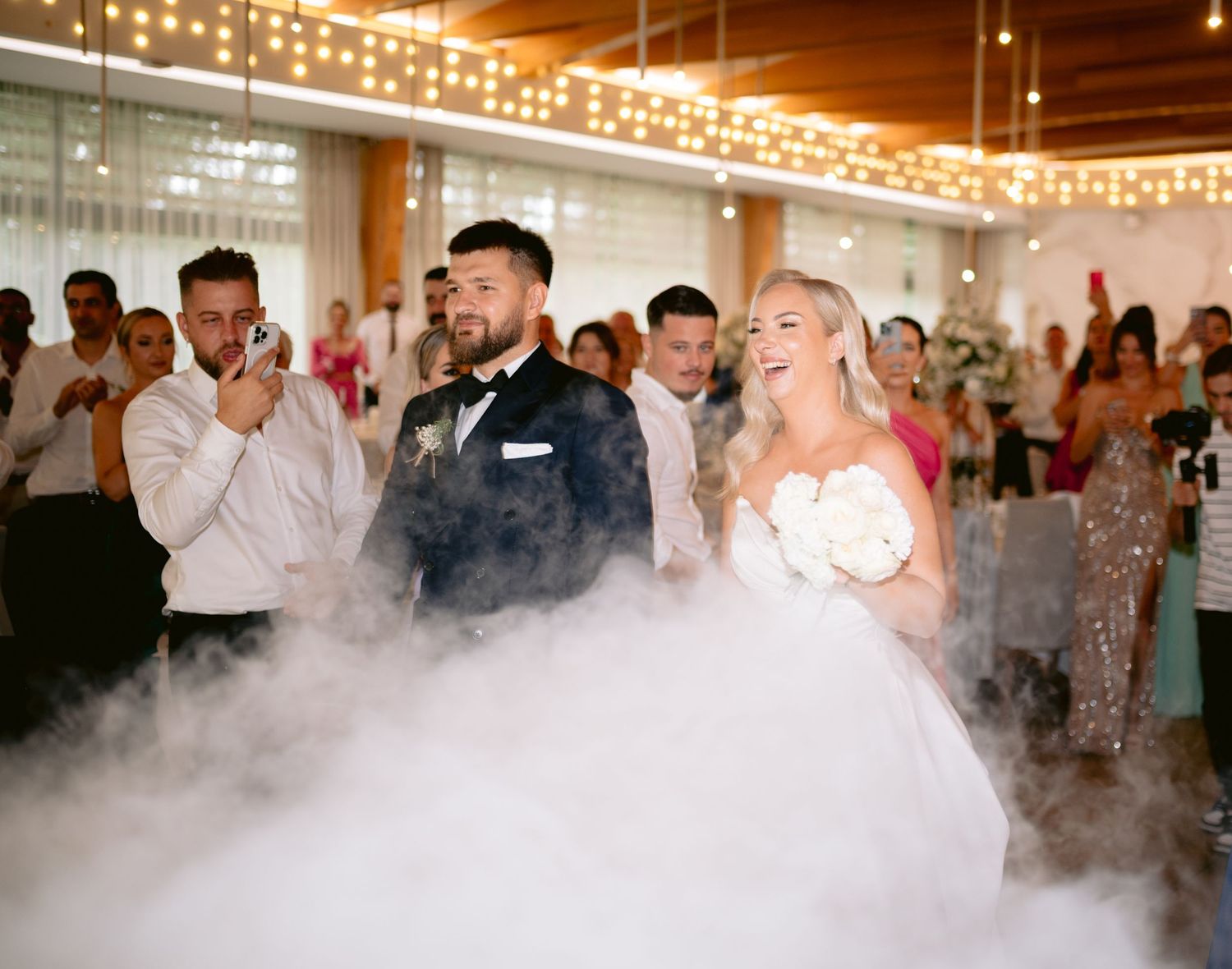 Bride and groom share first dance surrounded by dramatic fog machine smoke at elegant wedding reception venue.