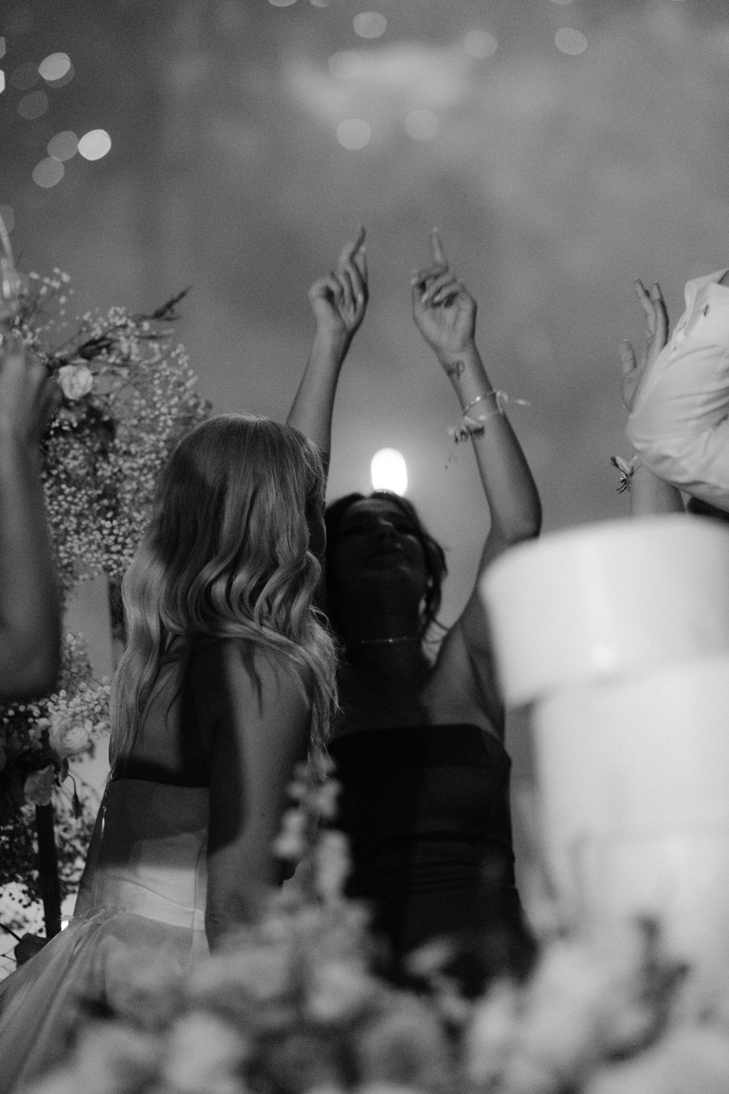 Black and white photo of women dancing with arms raised at an elegant wedding reception with floral arrangements.