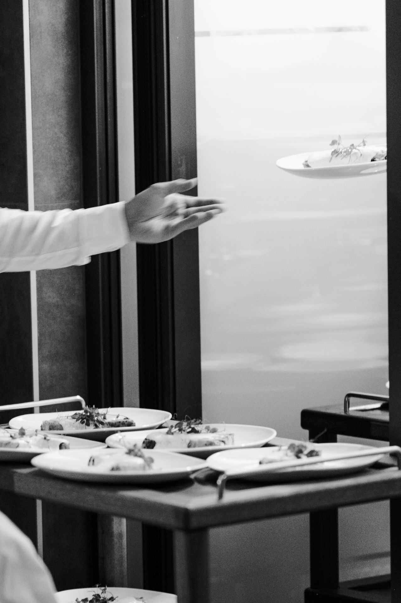 Black and white image of restaurant servers carrying multiple plates of food through a dining room.